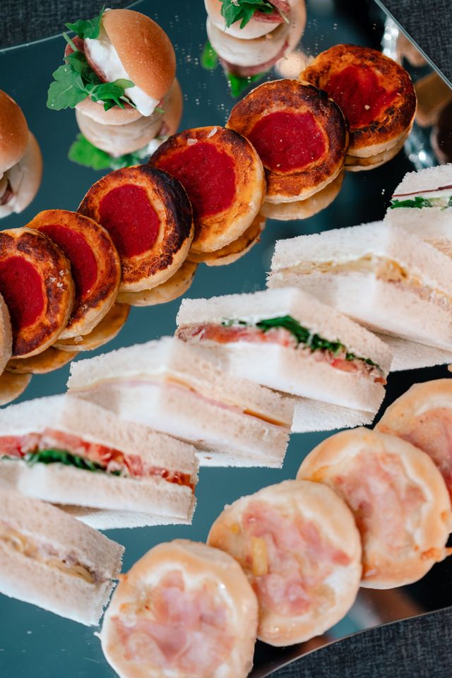 Un assortimento di stuzzichini monoporzione disposti su un piatto, tra cui panini, piadine arrotolate e tartine con guarnizione rossa.
