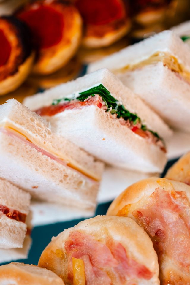 Un assortimento di tramezzini e pasticcini su un vassoio, tra cui tramezzini triangolari senza crosta con ripieni colorati.