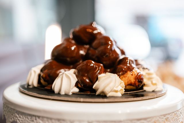 Piatto di pasticcini ripieni di crema e ricoperti di salsa al cioccolato, serviti su un'alzatina bianca.