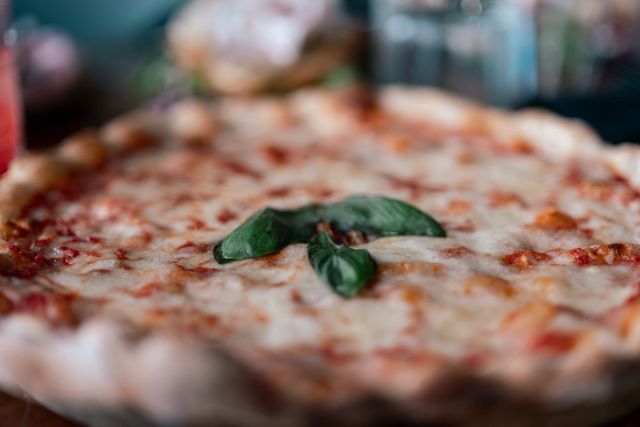 Primo piano di una pizza al formaggio con foglie di basilico su un tavolo.