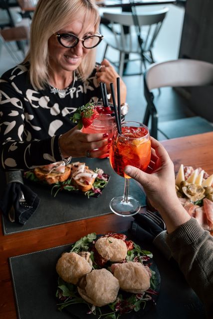 Due persone brindano con cocktail arancioni brillanti a un tavolo di un ristorante, accompagnati da patatine fritte e antipasti.
