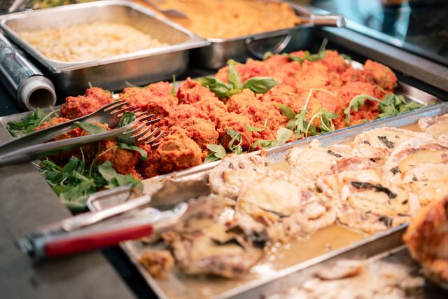 Vassoi da buffet con piatti misti, tra cui alimenti rossi e beige cremosi sminuzzati, con pinze da portata.