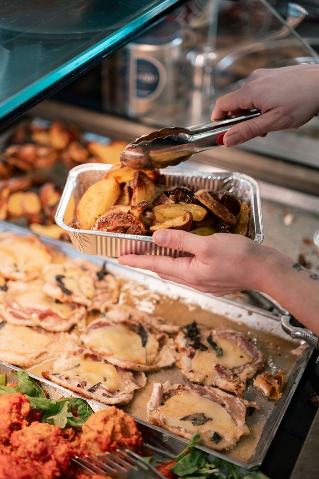 Mani che servono patate arrosto da un vassoio da buffet accanto ad altri piatti caldi.