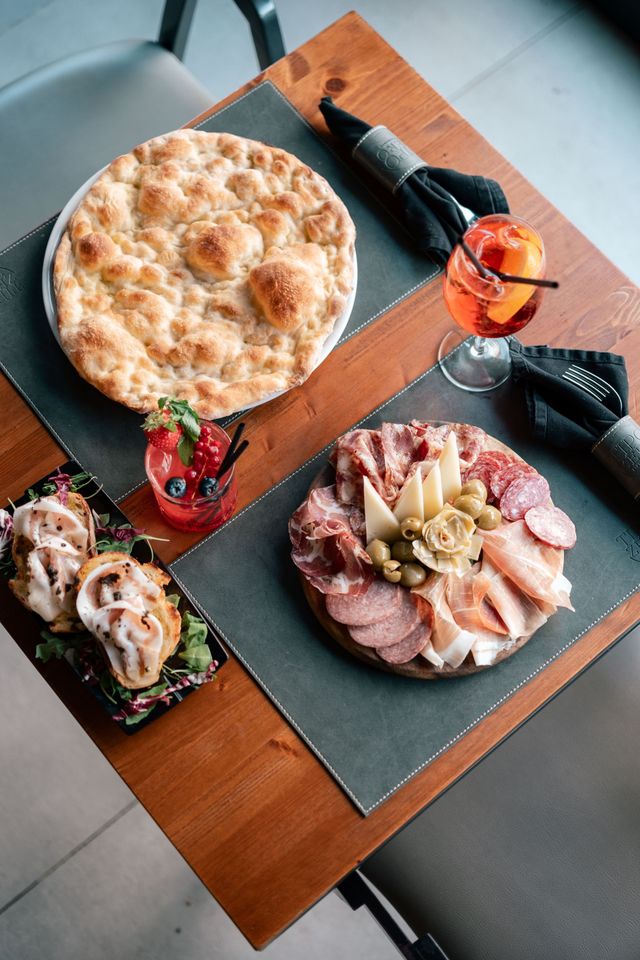 Un assortimento di pizze e focacce su un tavolo di legno, con bevanda e posate.