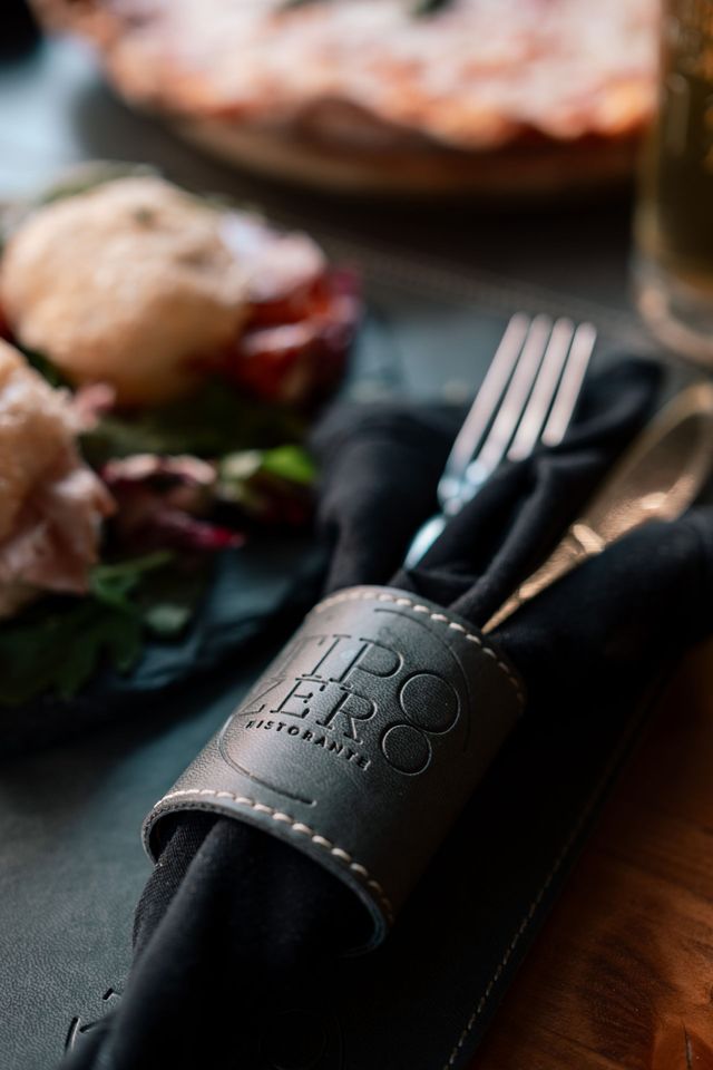 Elegante apparecchiatura con tovagliolo nero, posate e anello portatovagliolo in pelle su un tavolo da pranzo.