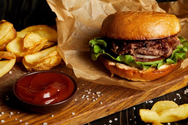 Hamburger con patatine fritte e ketchup su un tagliere di legno, avvolto nella carta.