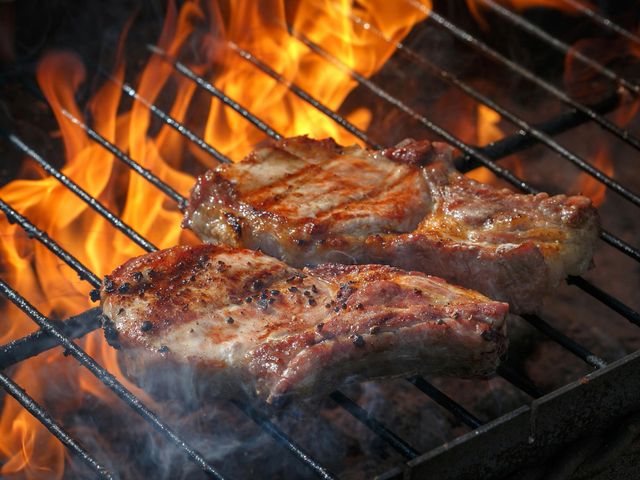 Due bistecche grigliate sulle fiamme di un barbecue, con il fumo che sale.