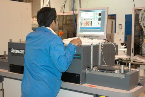 A technician in a blue lab coat operates a Sewscan industrial scanning system in a workshop environment.
