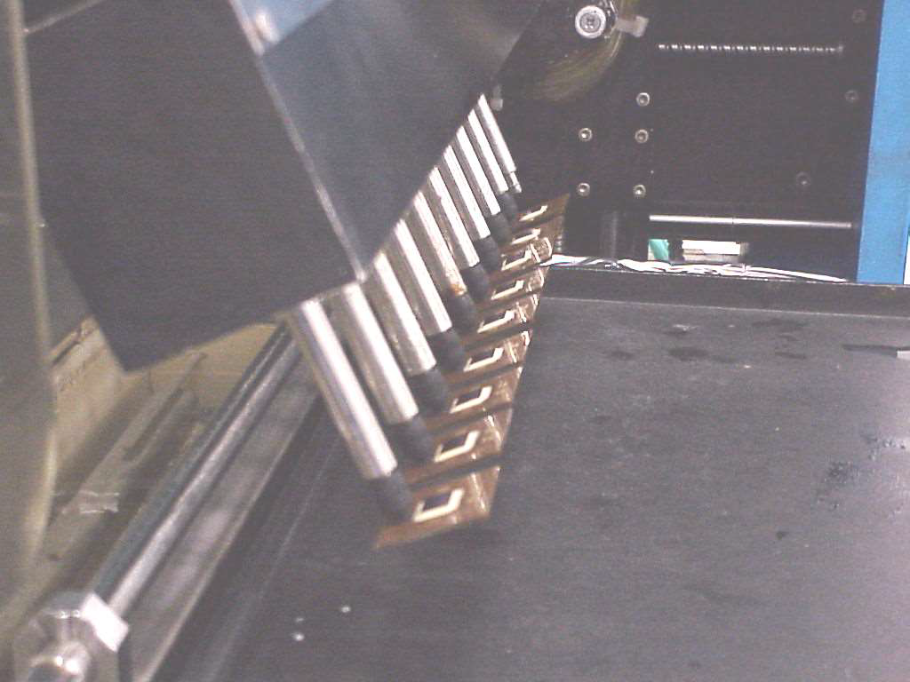 An industrial machine with a row of metal robotic arms placing small components onto a dark conveyor belt.