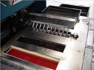 Metal machinery with black and red openings and a row of rollers on a stainless steel surface