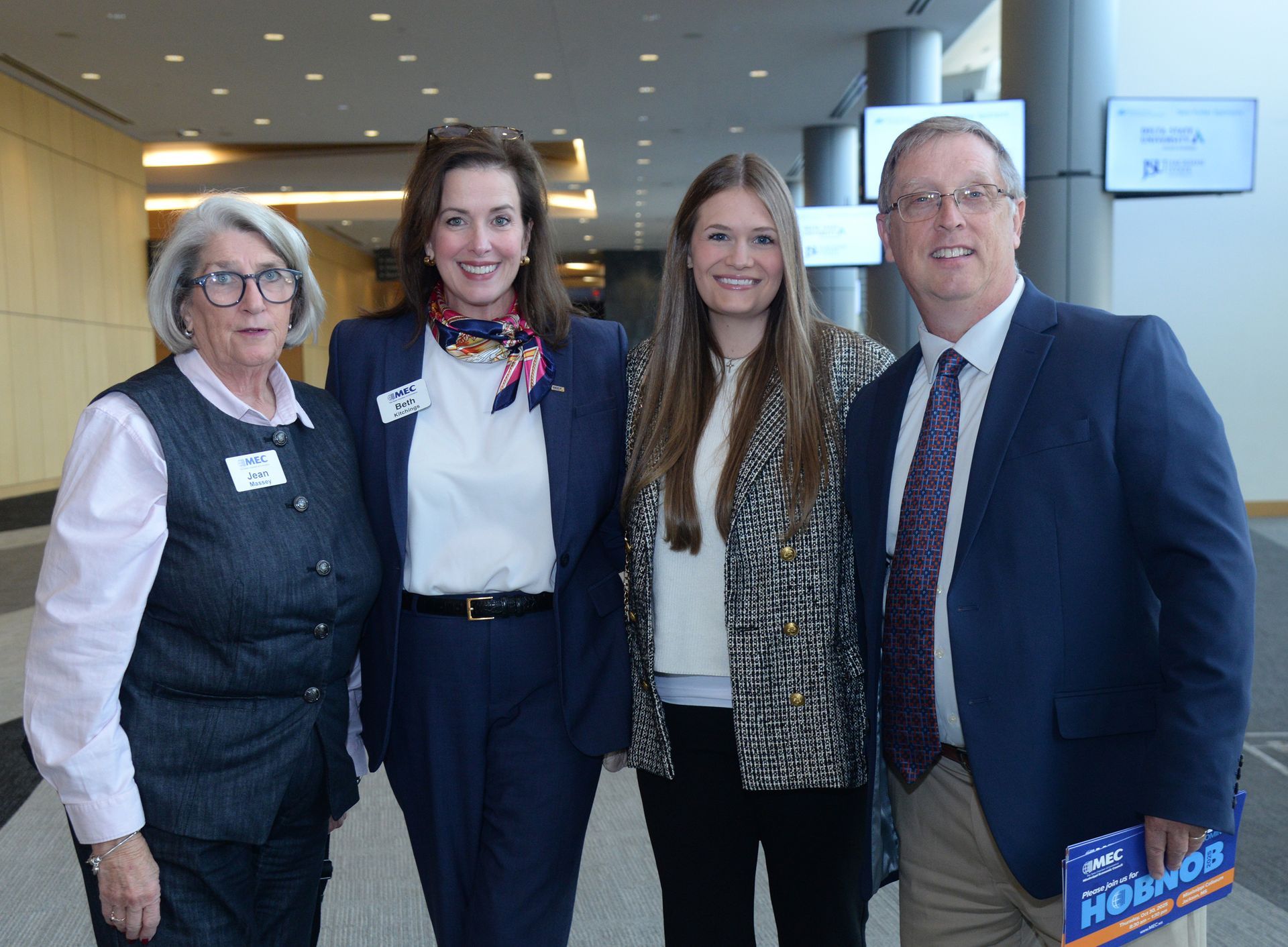 Four people pose inside a building. Two women and two men smile, wearing business attire.