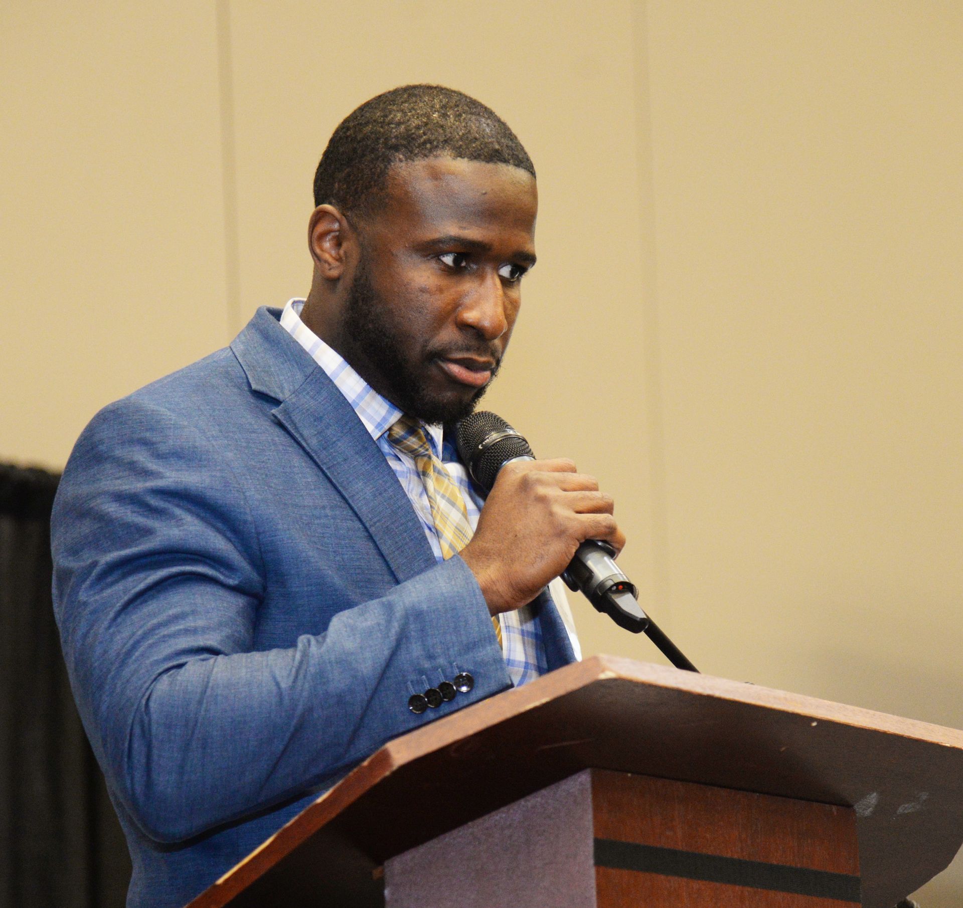 Man in blue blazer speaking at a podium, holding a microphone.