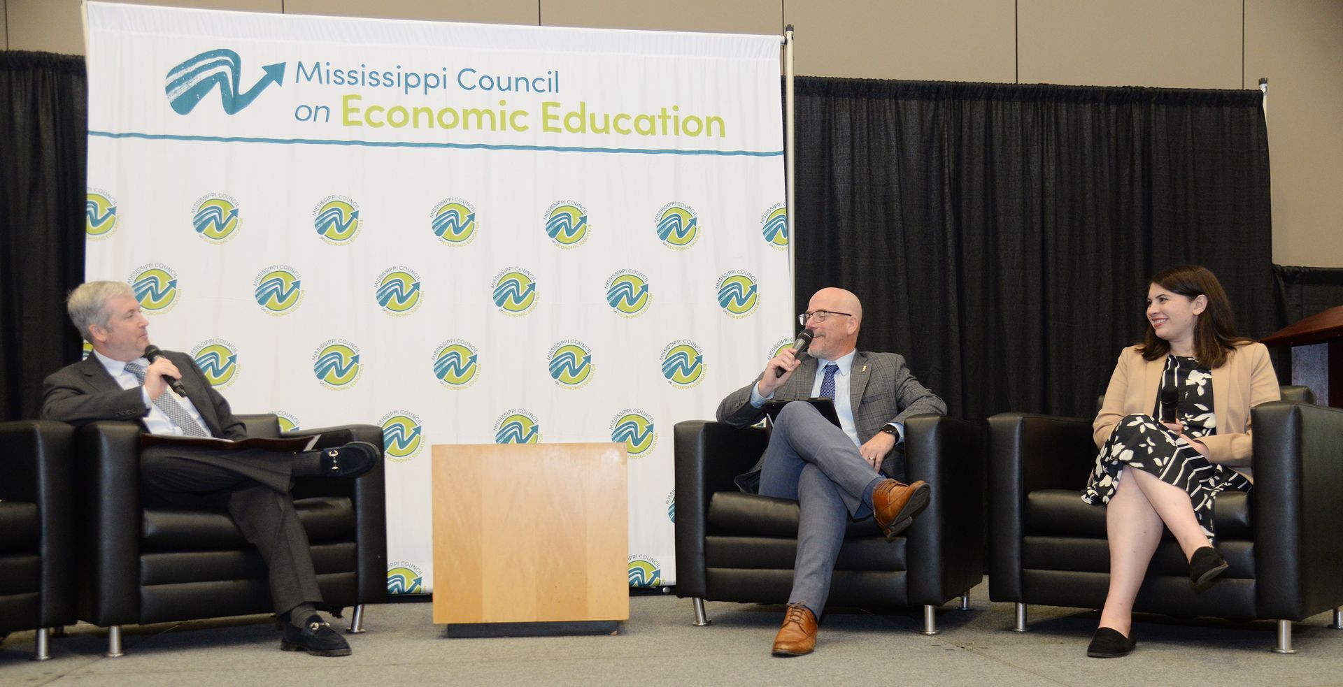 Three people sit on a panel at an event for the Mississippi Council on Economic Education.