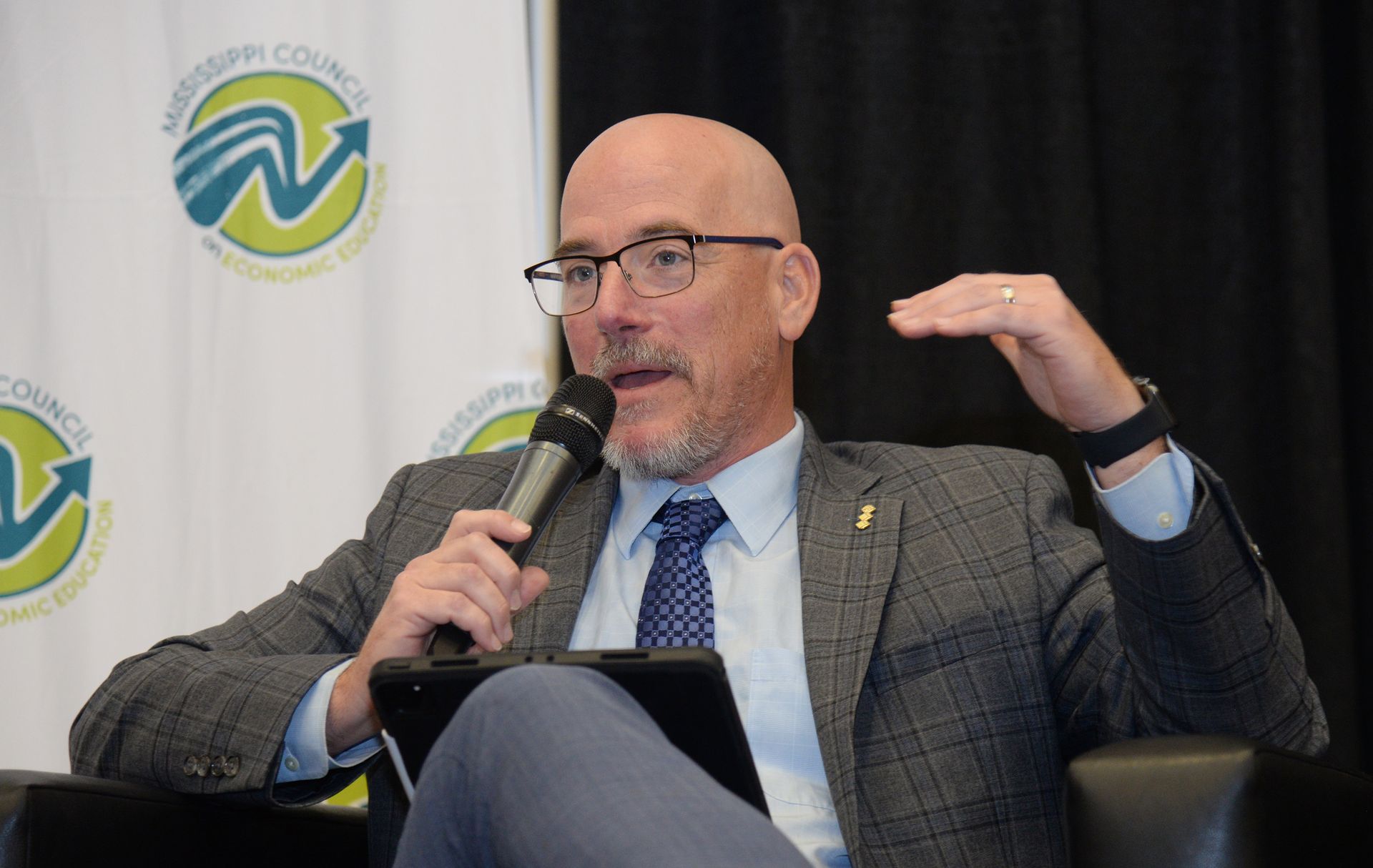 Man speaking into a microphone, gesturing with his hand during a panel discussion.
