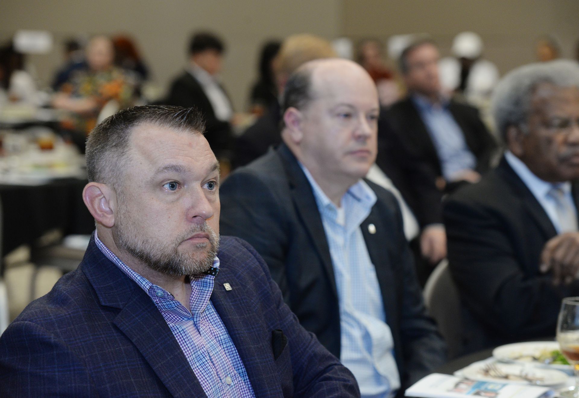 Men in suits at a conference, some looking attentively forward.