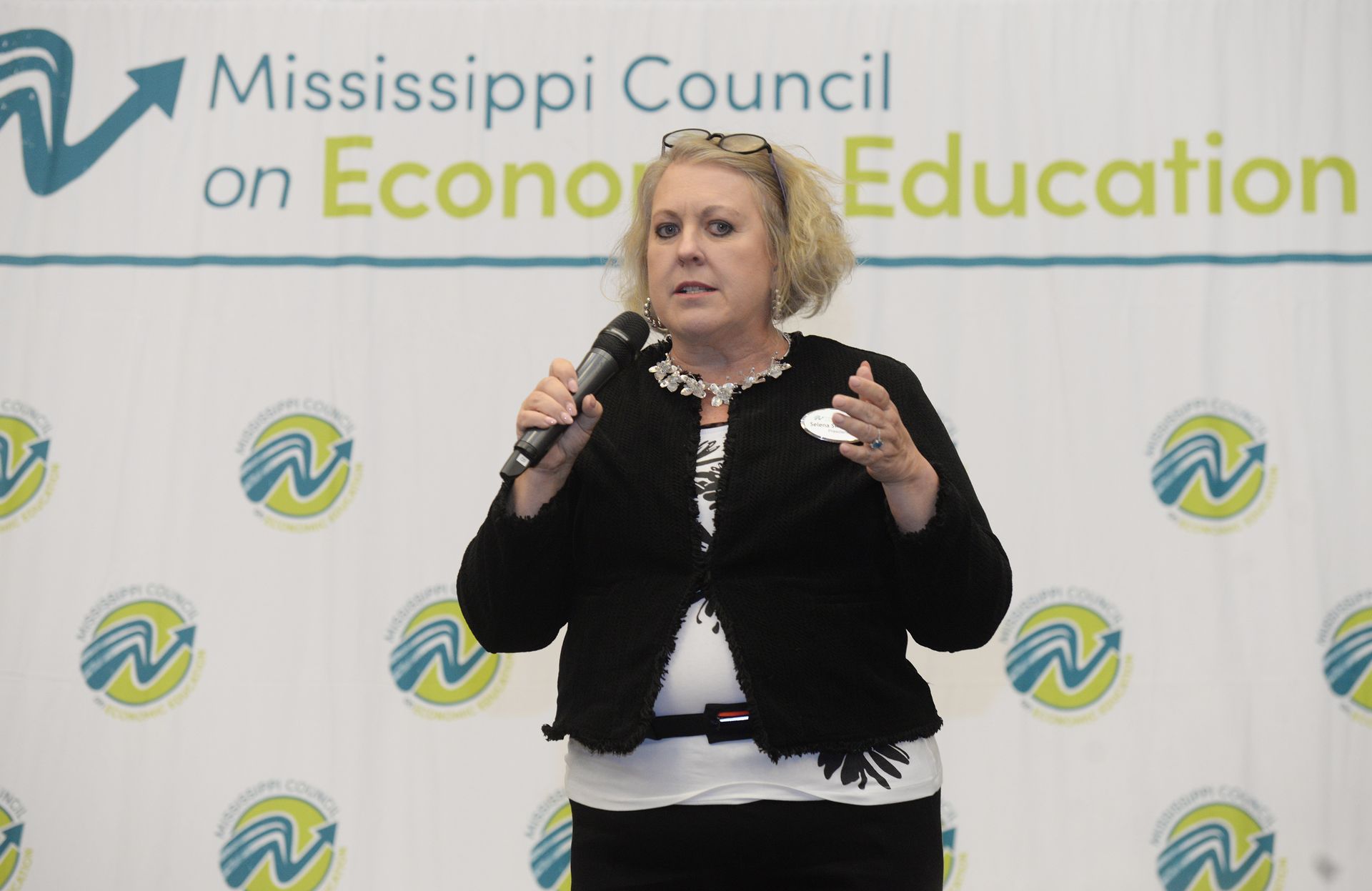 Woman speaking into a microphone at an event for the Mississippi Council on Economic Education.