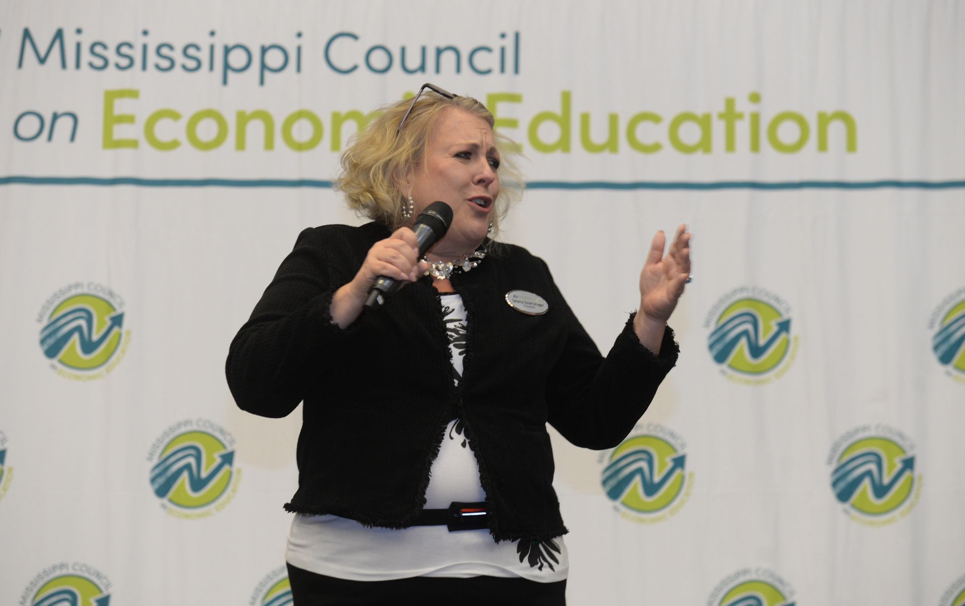 Woman speaking into a microphone at an event for the Mississippi Council on Economic Education.