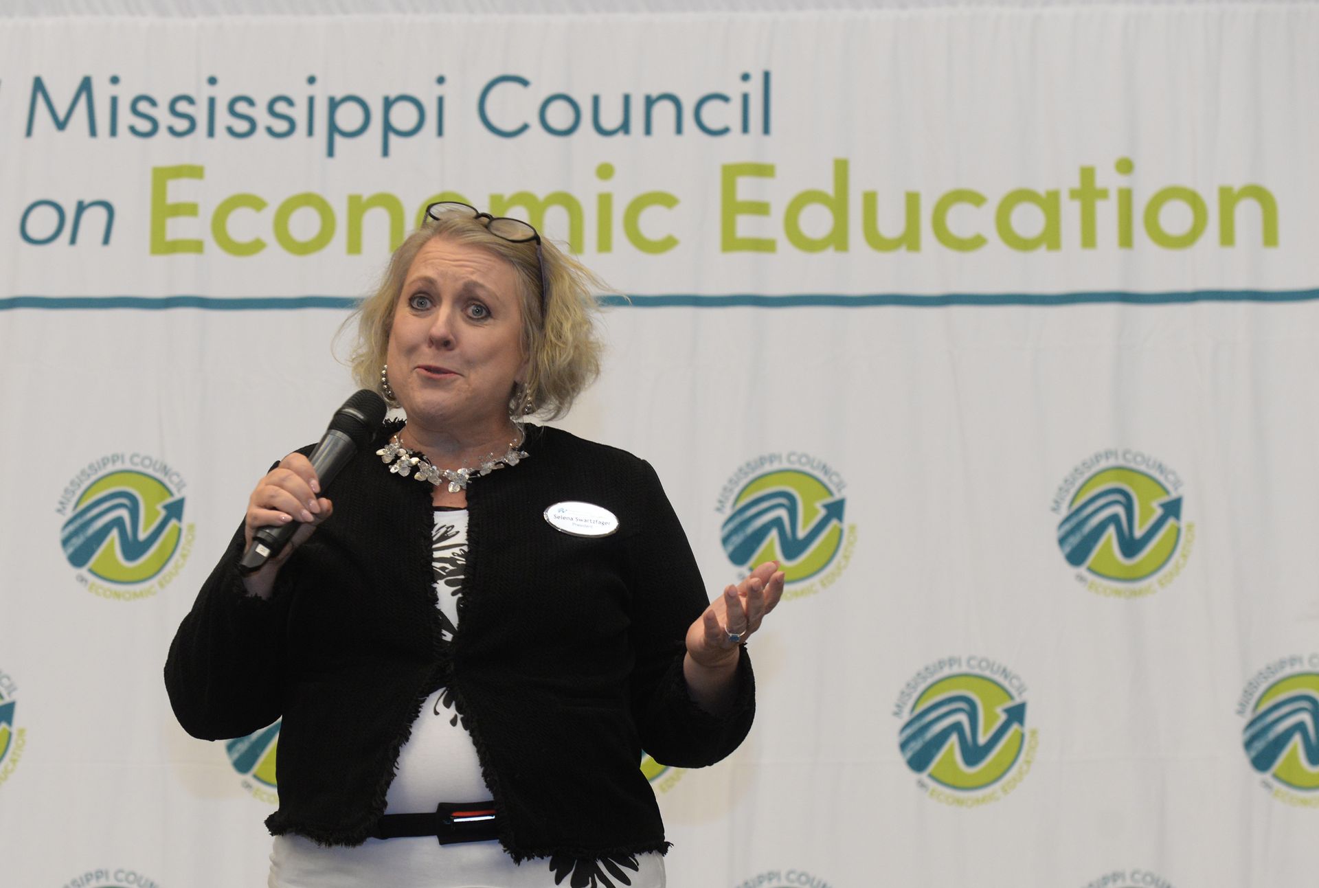 Woman speaking into a microphone at an event for the Mississippi Council on Economic Education.