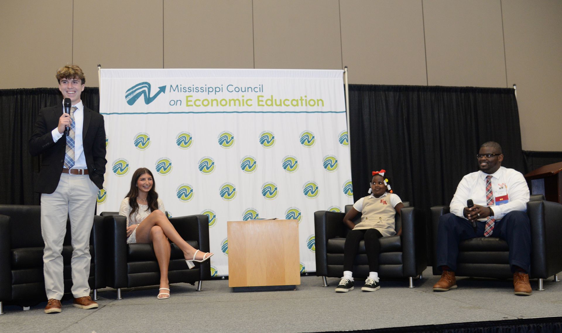 Panel of four people on stage with banner of Mississippi Council on Economic Education.