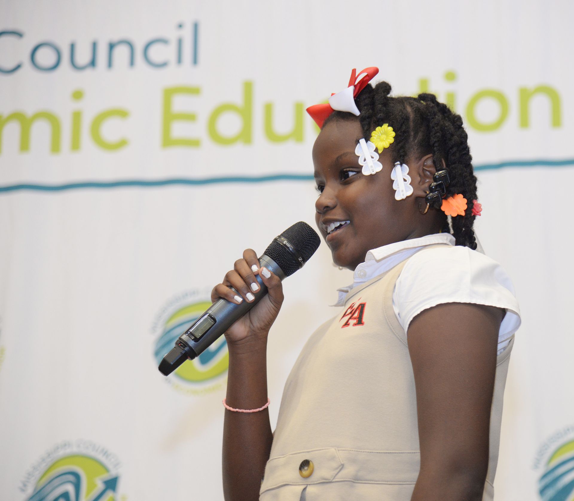 Young girl speaking into a microphone at an event, wearing a uniform.