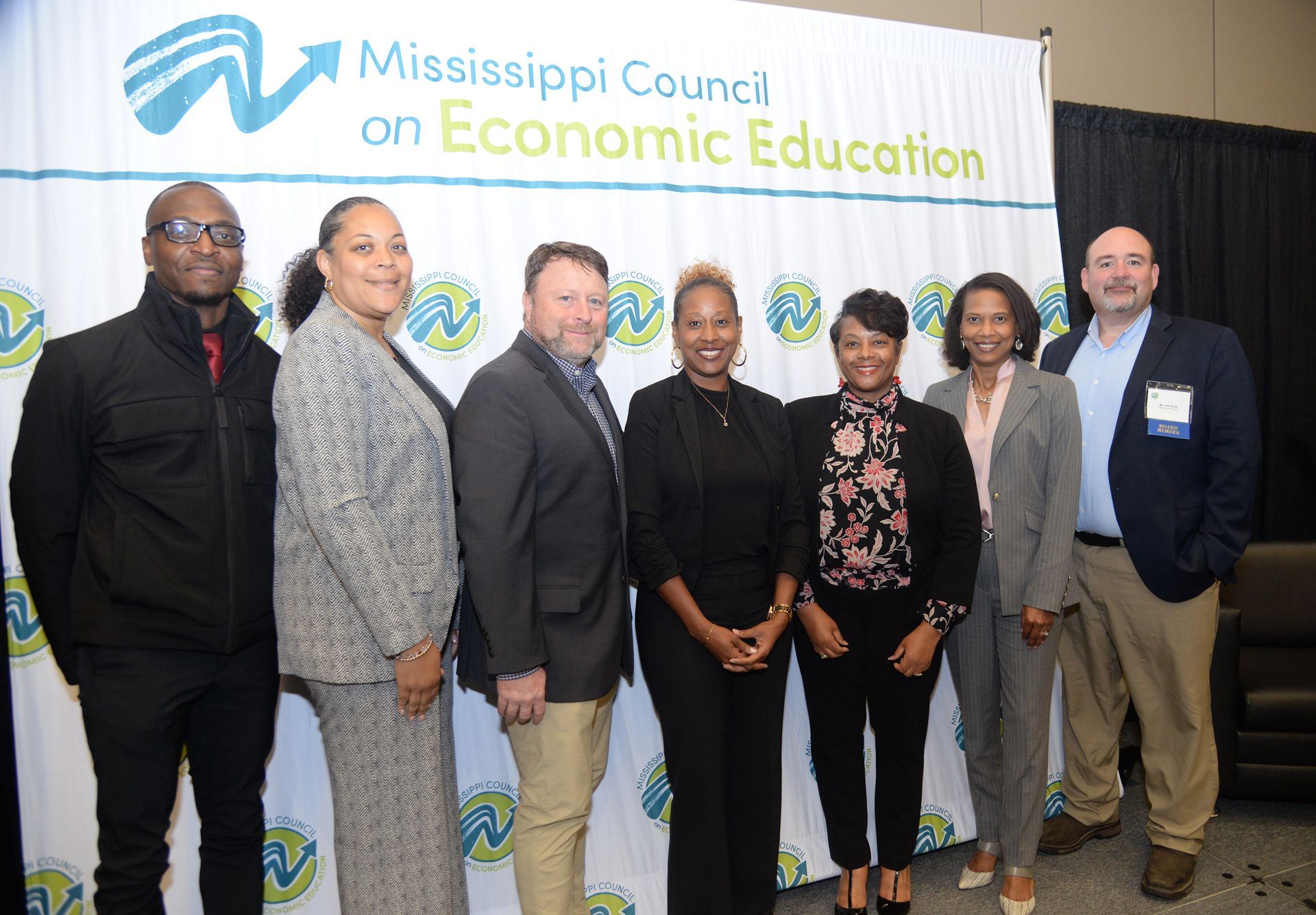 Group of people posing in front of a conference backdrop. They are dressed in business attire.