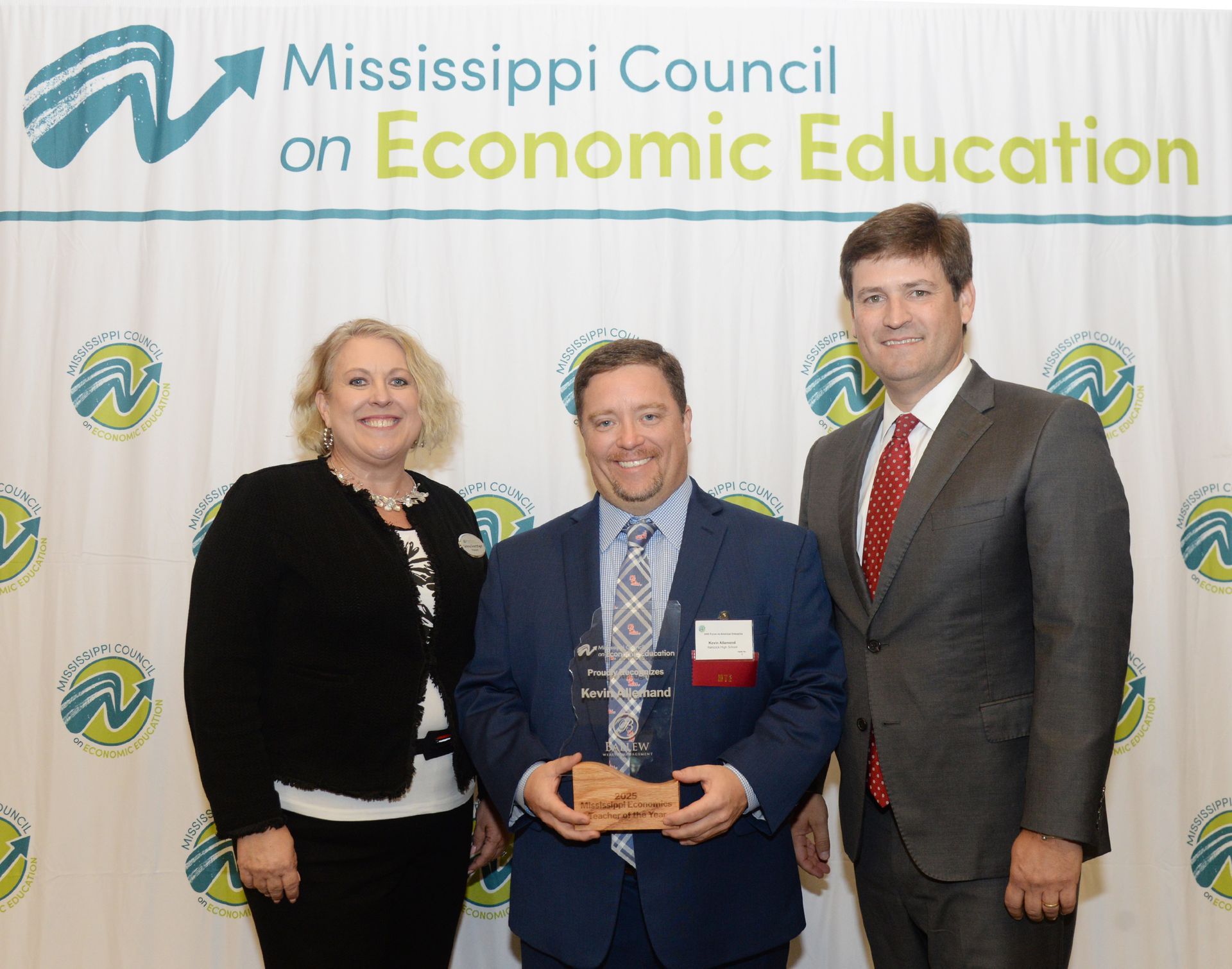 Three people posing, one holding an award, Mississippi Council on Economic Education background.