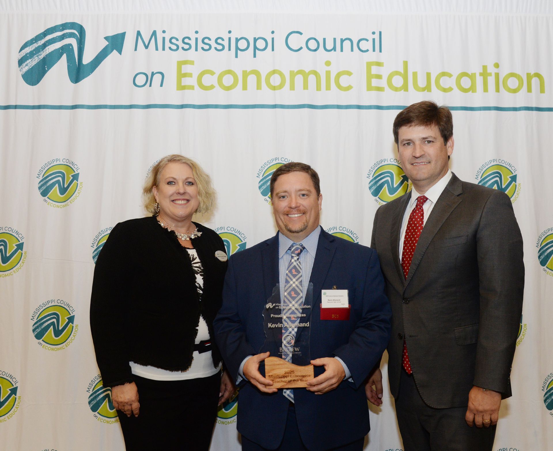 Three people pose with an award in front of a backdrop with the Mississippi Council on Economic Education logo.