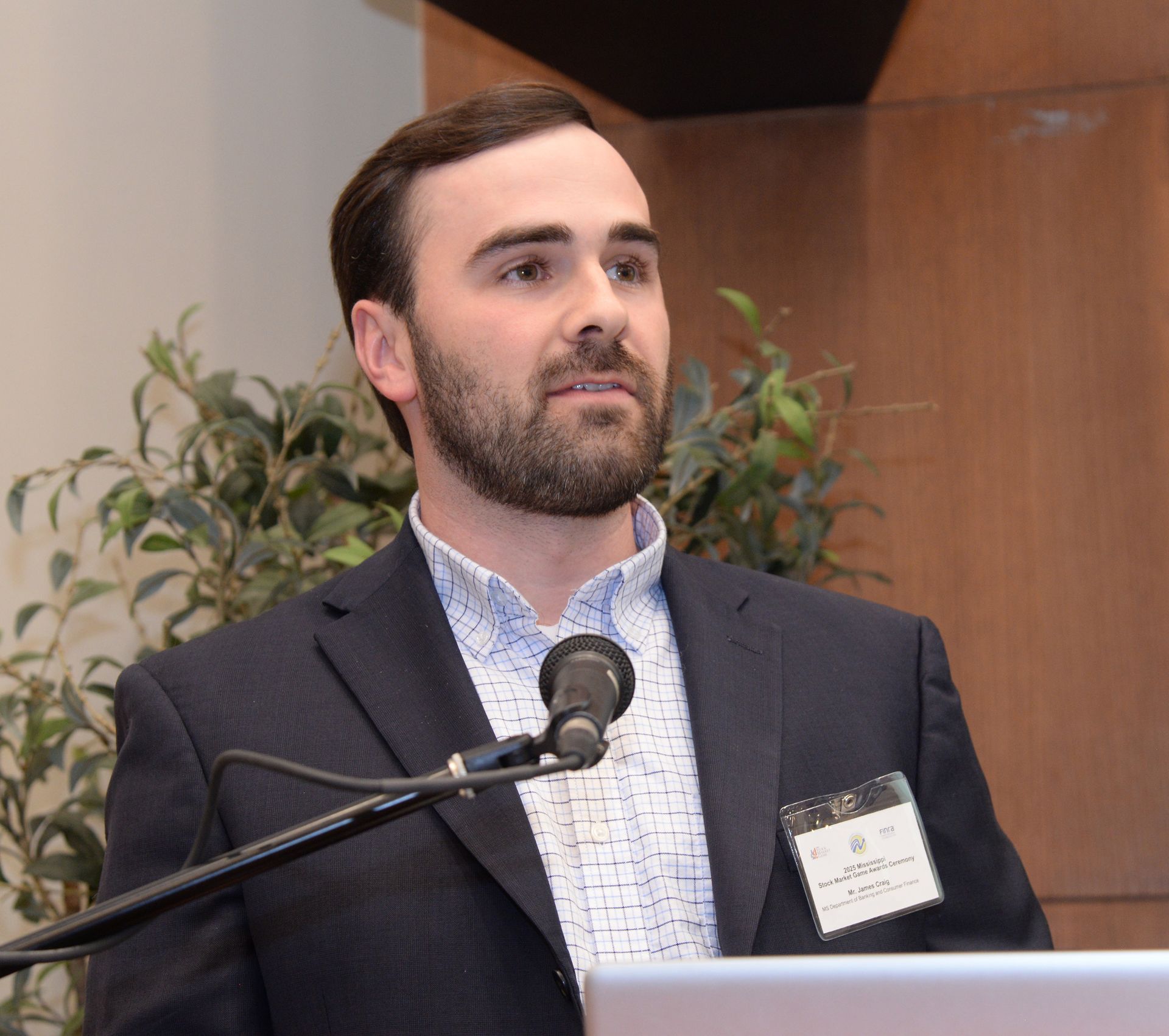 Man speaking at a podium, wearing a suit jacket and collared shirt.