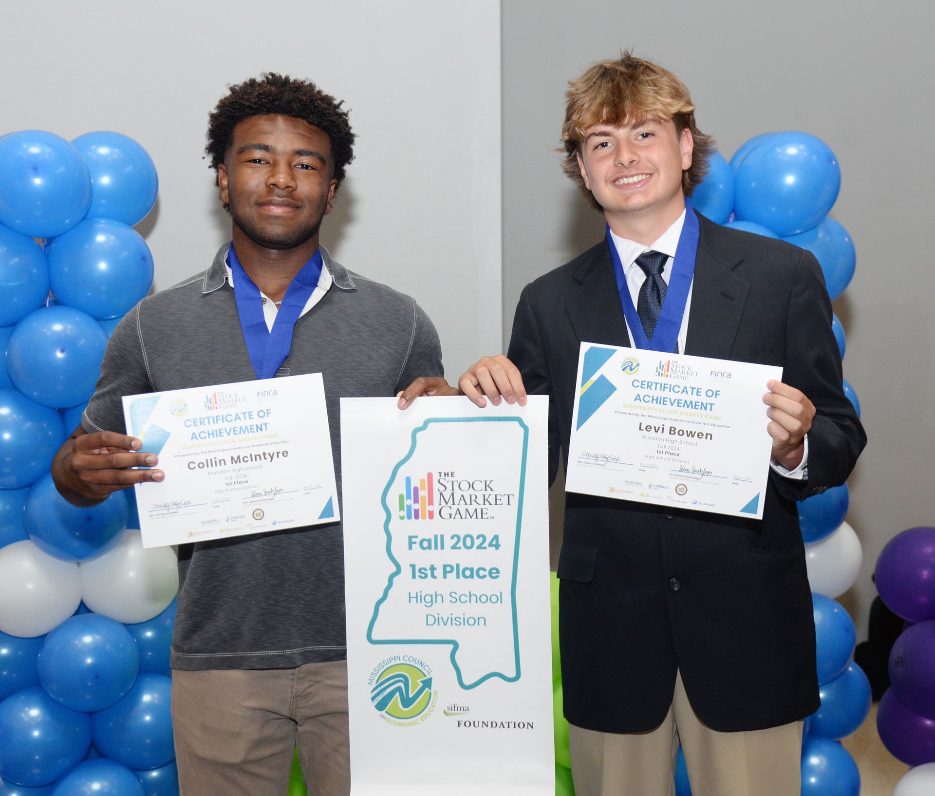 Two boys holding awards, standing in front of balloons.