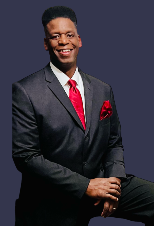 Man in a black suit with red tie and pocket square smiles, leaning forward.