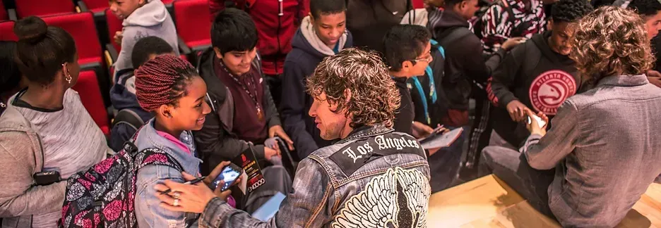 People in a theater, some are speaking to a man wearing a denim jacket.