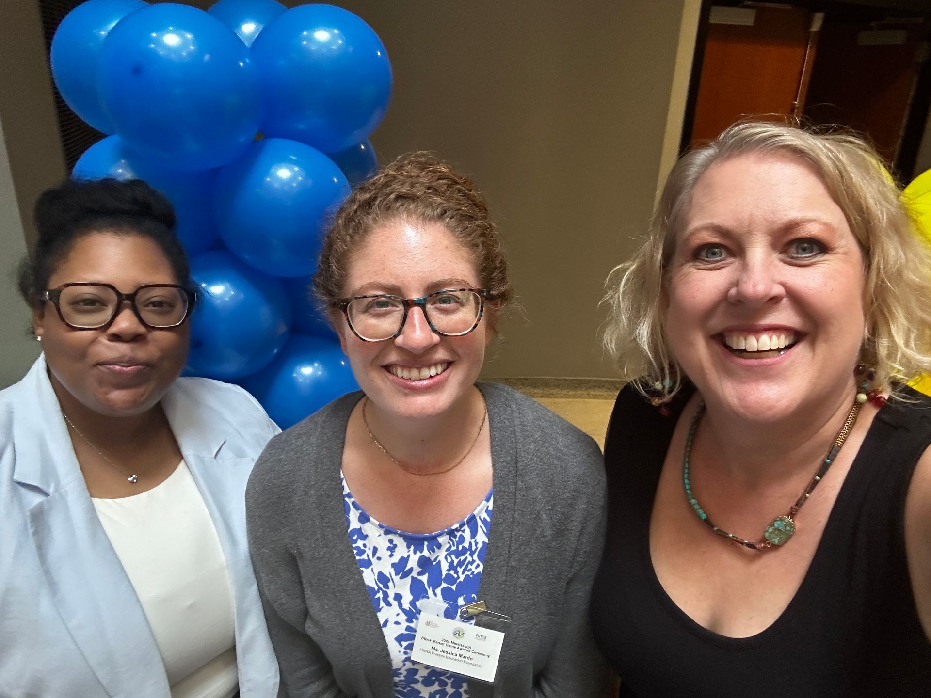Three smiling people pose in front of blue balloons.