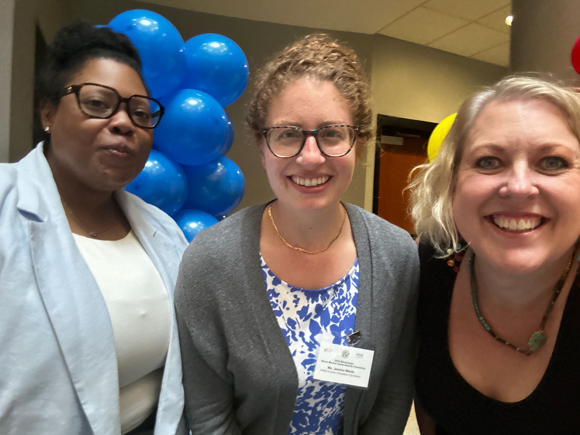 Three smiling people with blue balloons in the background.