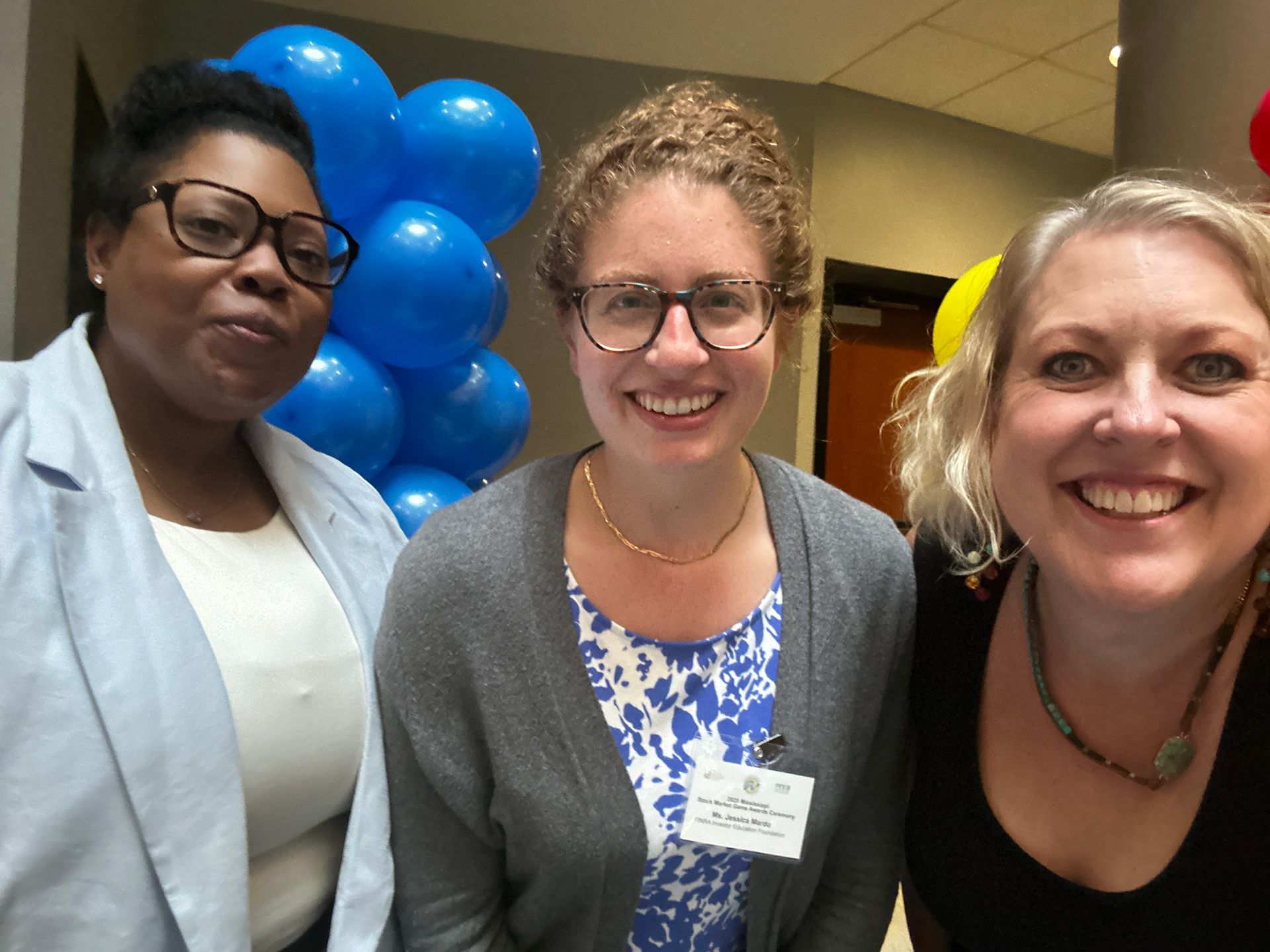 Three smiling people pose for a photo in front of blue balloons.
