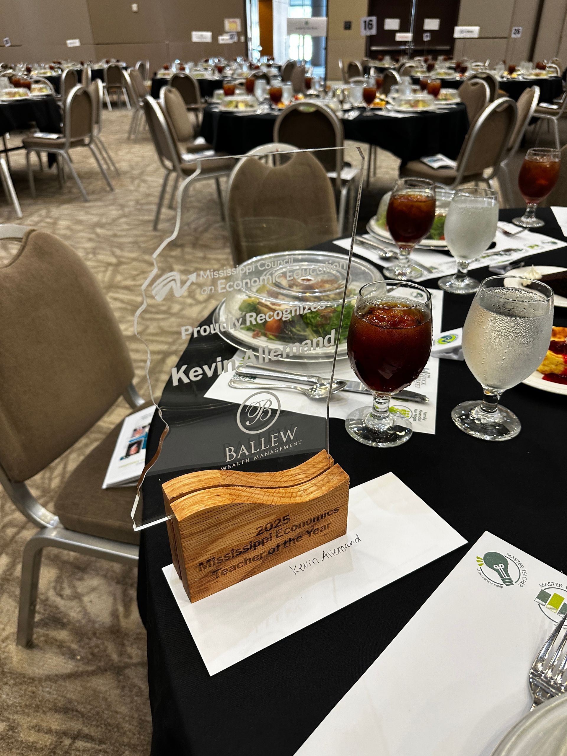 Event tables set for a meal, with glassware, food, and decorative awards.