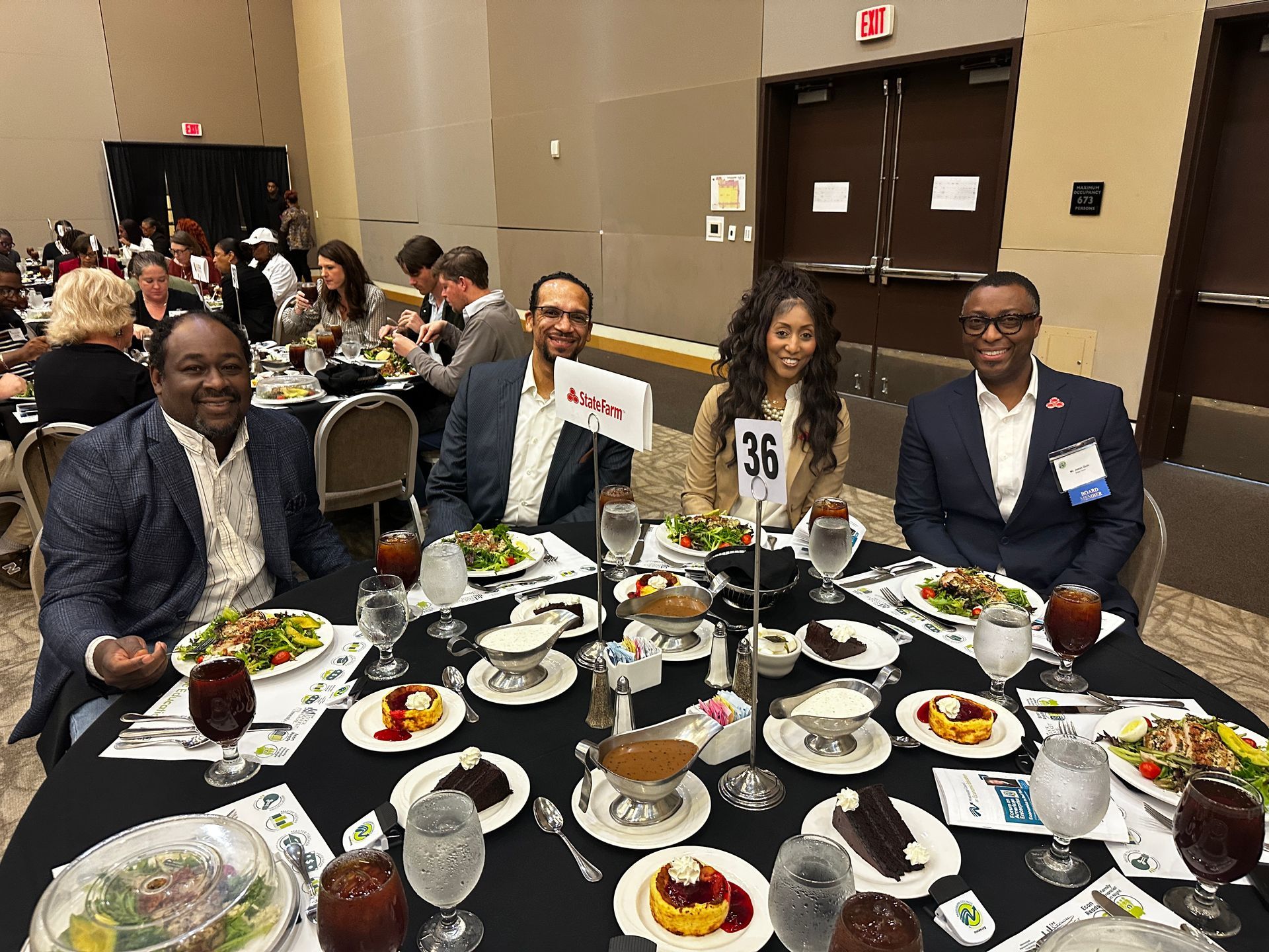 Four people seated at a table, eating at a formal event. Food and drinks are present.