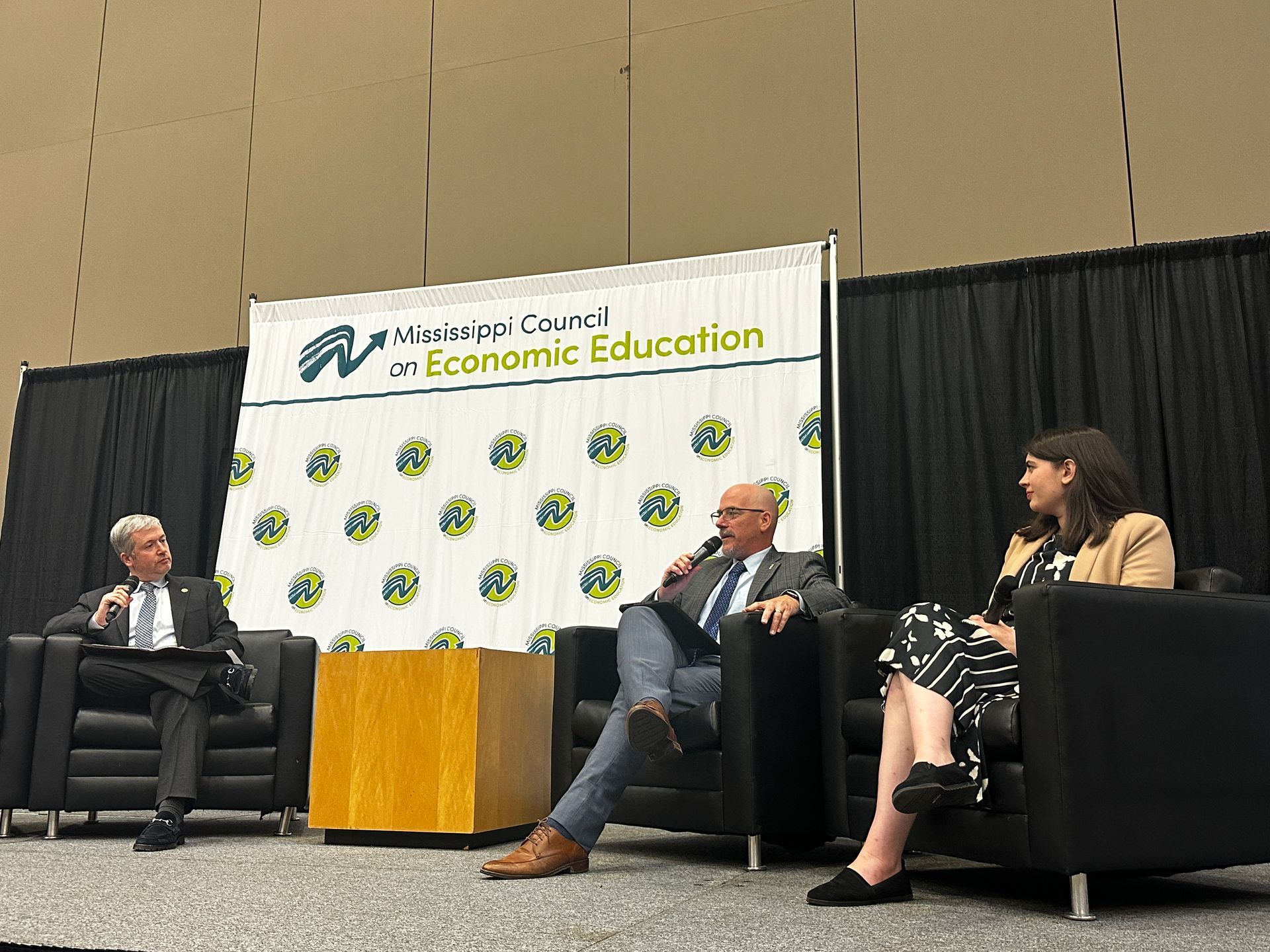 Panel discussion on stage with three people seated. Banner in background.