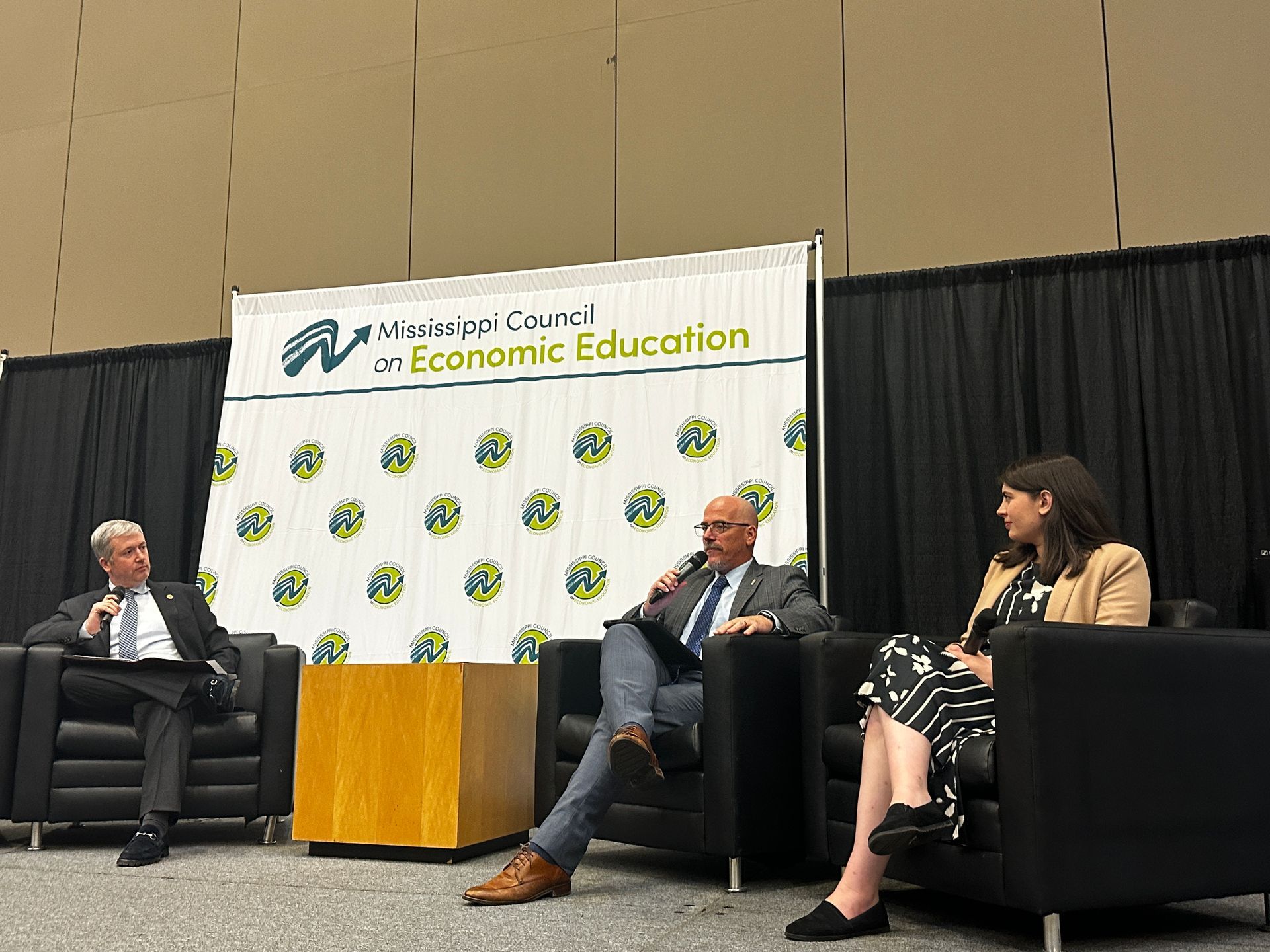 Panel discussion at the Wisconsin Council on Economic Education. Three people on stage, one speaking with a microphone.