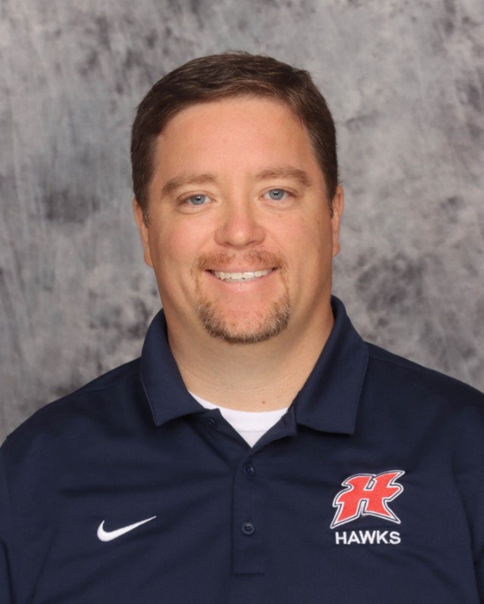 Man smiling, wearing a navy blue polo shirt with a red 