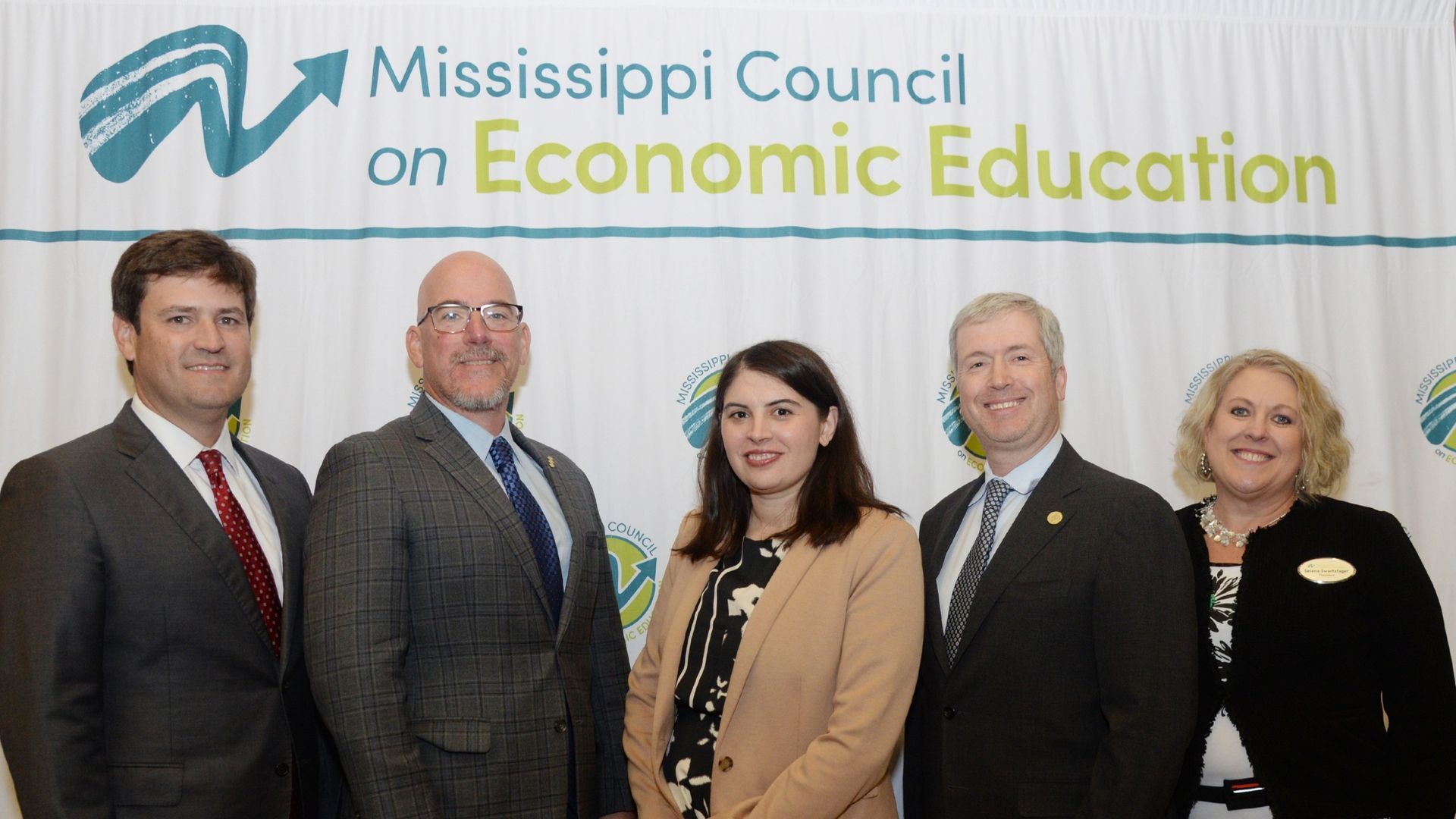 Five people pose in front of a banner for the Mississippi Council on Economic Education.