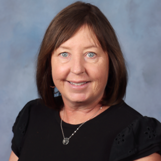 Woman with brown hair and blue eyes, smiling, wearing a black top, against a blue background.