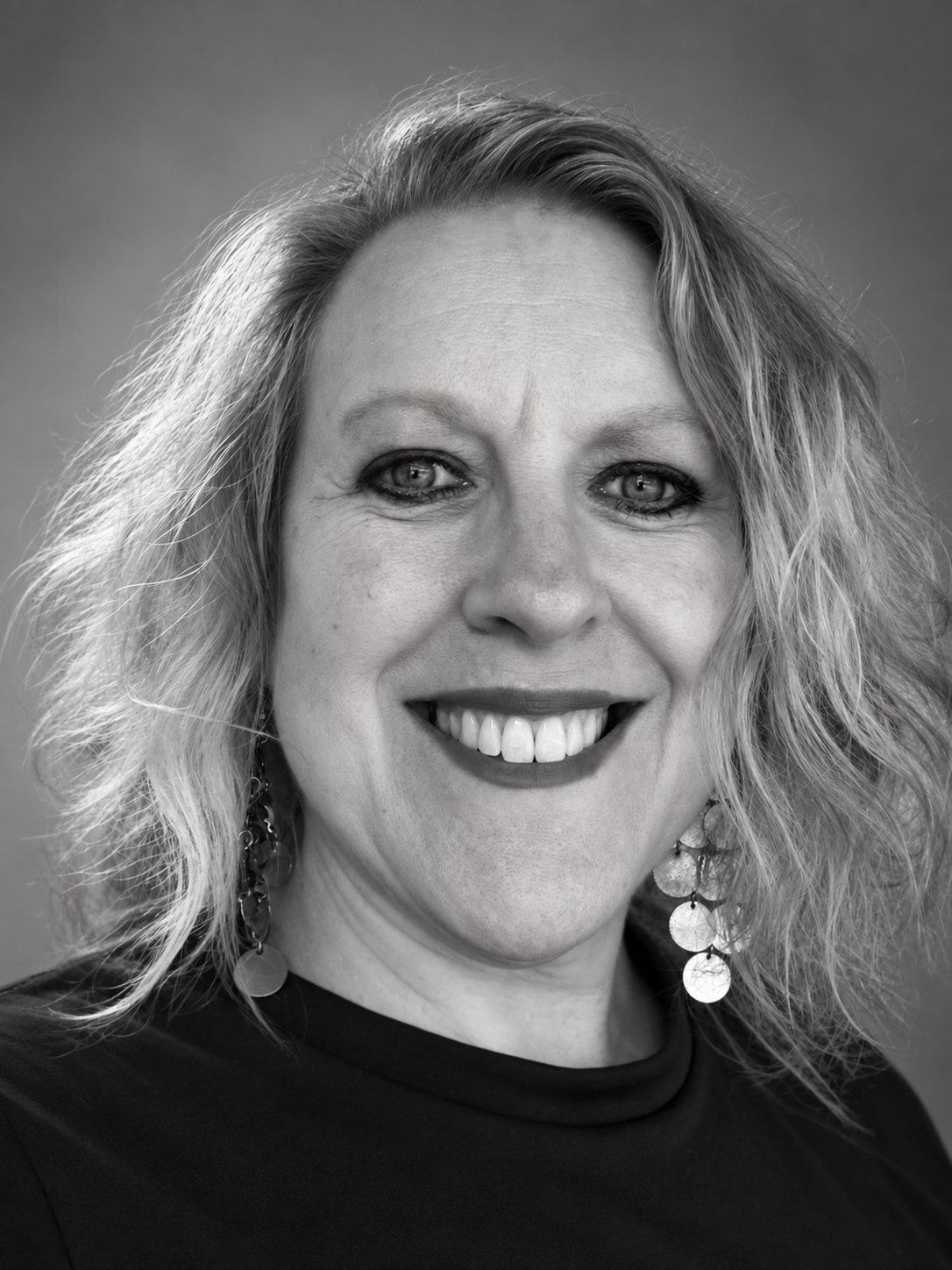 A woman wearing a blue shirt and a necklace is smiling for the camera.