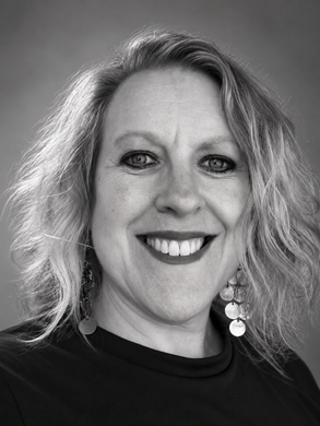 A woman wearing a blue shirt and a necklace smiles for the camera