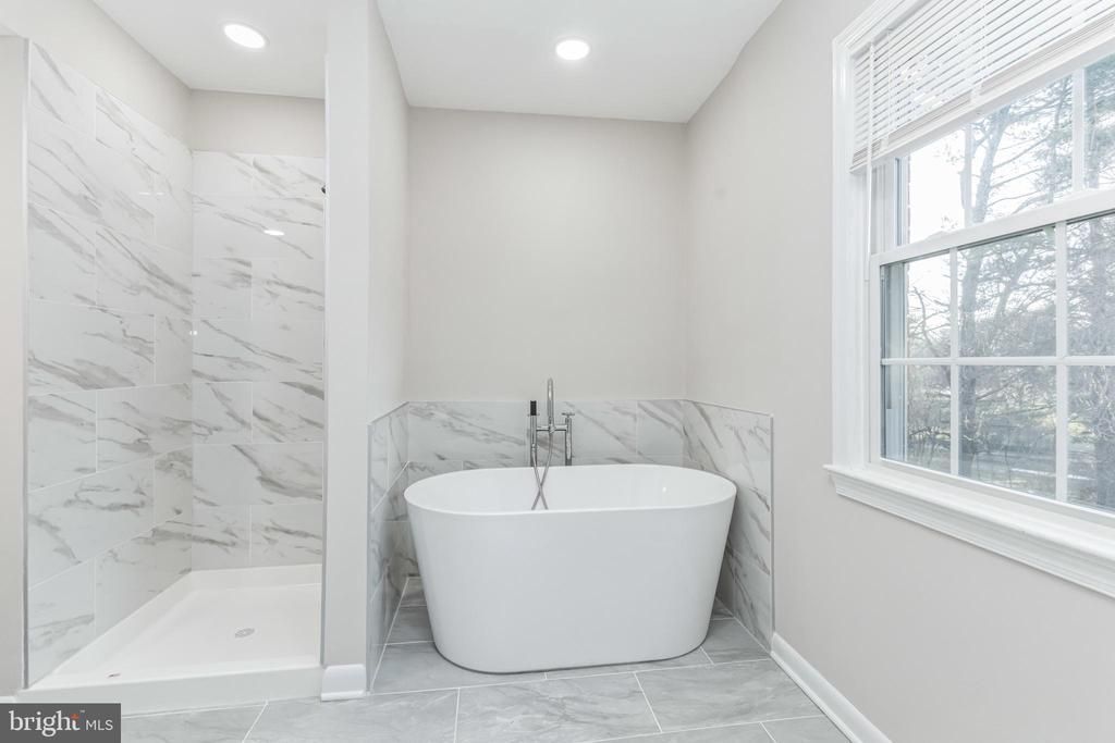 Modern white bathroom with freestanding tub, marble shower, and window overlooking greenery