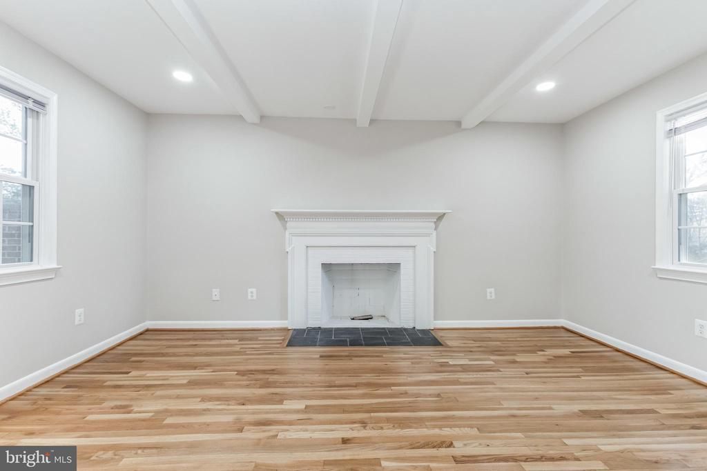 Bright empty living room with hardwood floors, white walls, and a fireplace centered on the far wall.