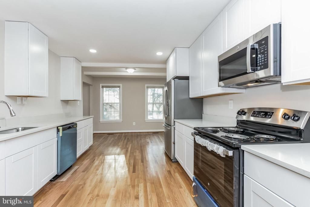 Bright white galley kitchen with stainless appliances, wood floors, and windows at the far end