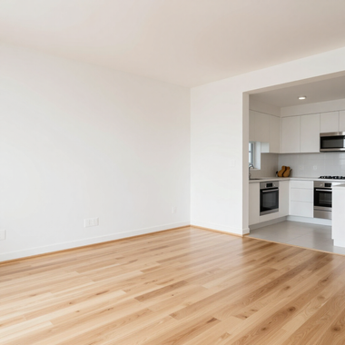 Empty white living room with light wood floors opening to a bright modern kitchen