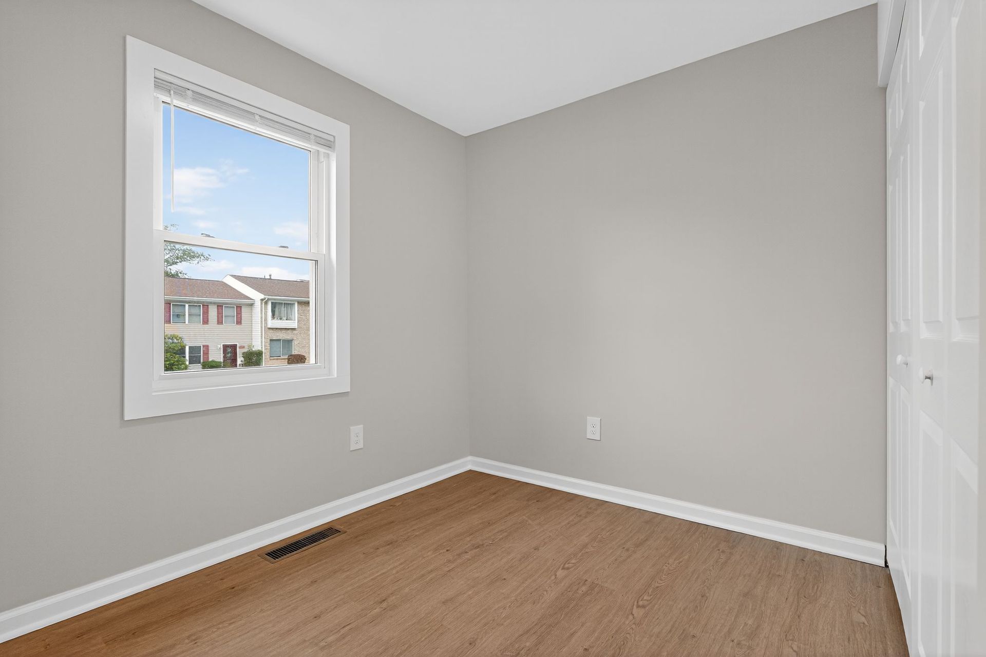 Empty gray bedroom with a window, white trim, and wood flooring