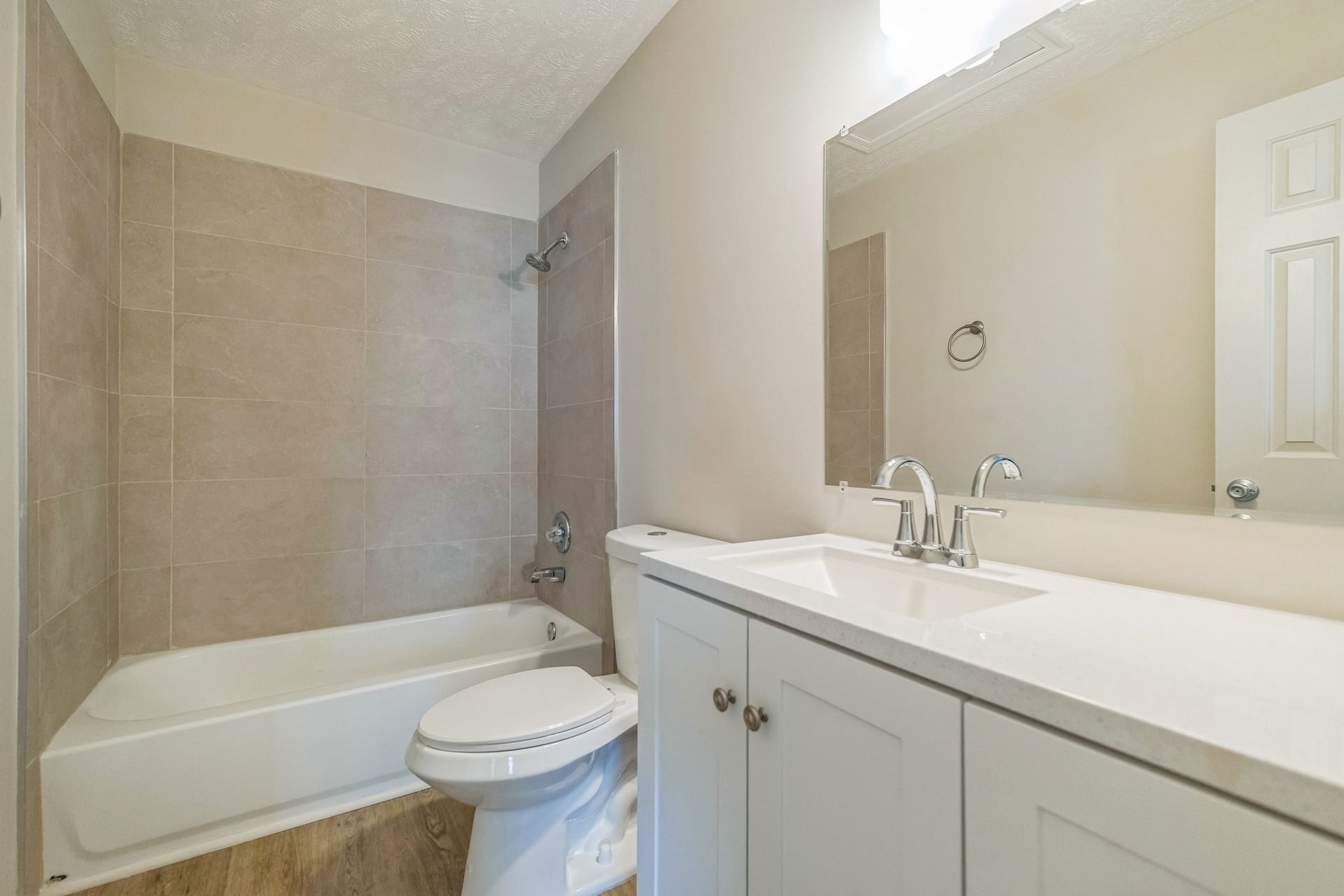 Bright bathroom with white vanity, large mirror, and beige tiled tub-shower combo.