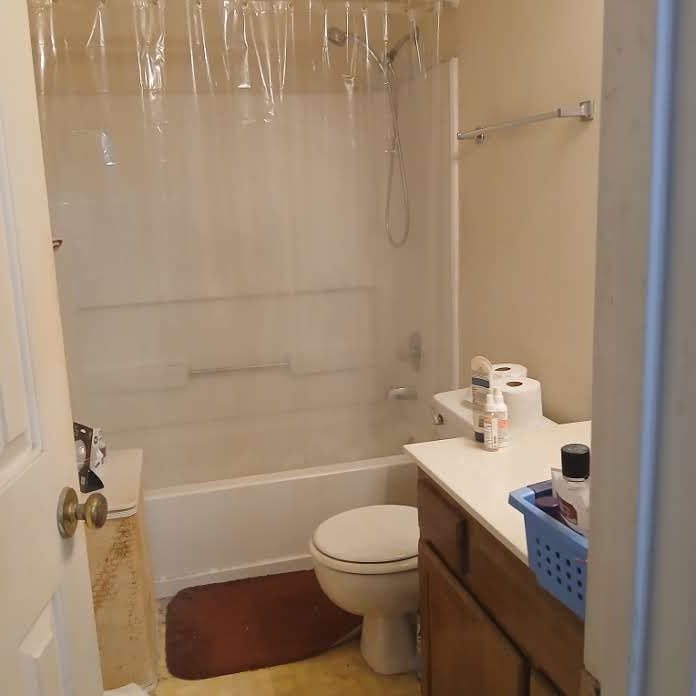 Small beige bathroom with tub-shower, toilet, sink vanity, and a brown bath mat.